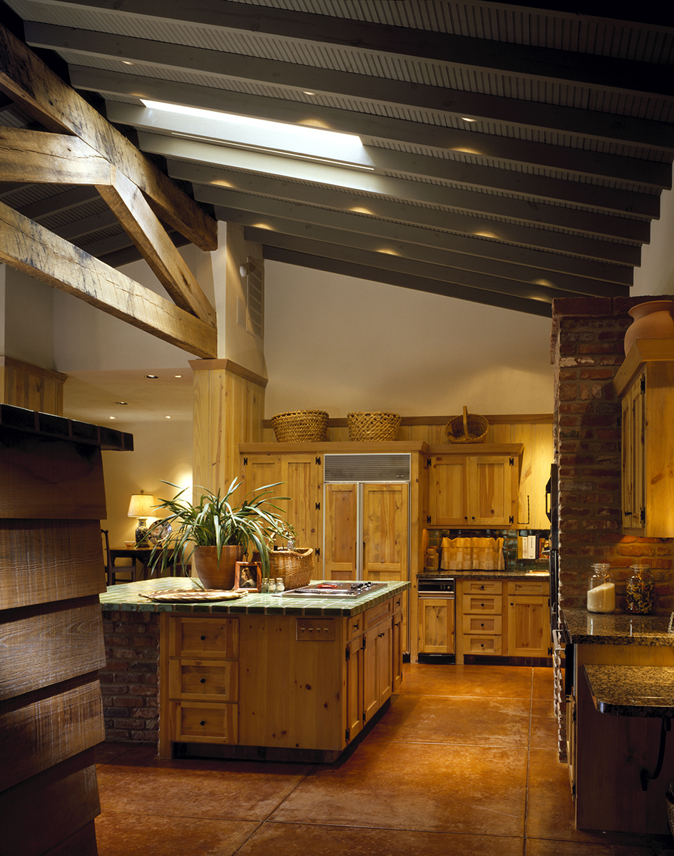 Rustic kitchen at REIF Residence featuring wood-burning stove, exposed timber ceilings, beadboard paneling, and scored concrete floors.