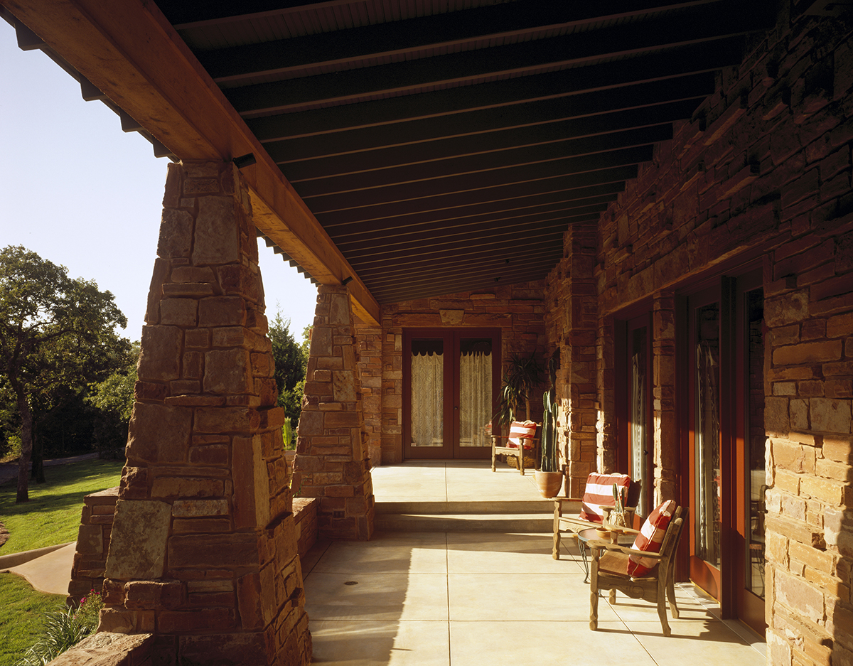 Expansive front porch of REIF Residence with natural stone base, timber columns, and shaded seating area overlooking the Oklahoma landscape.